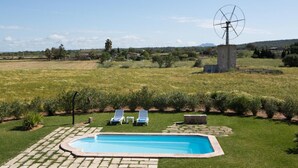 Une piscine avec des chaises longues, un moulin à vent et un champ d’herbe.