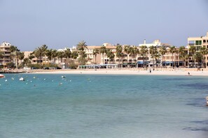 Un hotel frente al mar con vista a la playa, palmeras y cielo despejado.