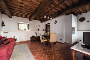 Una sala de estar acogedora con un sofá rojo, una mesa de comedor con sillas, un televisor y una zona de cocina con nevera y horno.