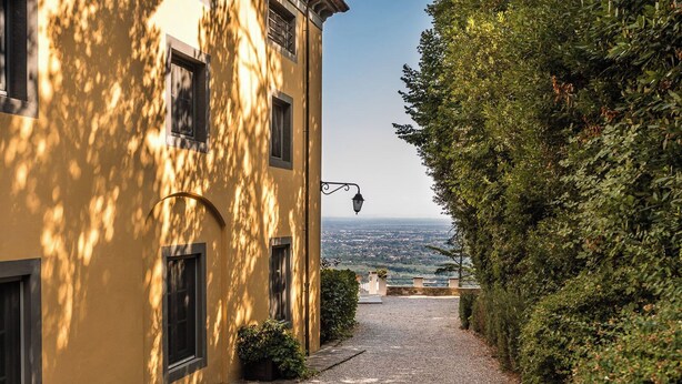 Un sentiero stretto di ghiaia conduce a un edificio con facciata gialla e numerose finestre.