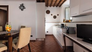 Una cucina compatta con mobili bianchi, un'area pranzo con tavolo e sedie, una TV e un orologio decorativo a parete.