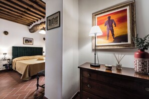 Una habitación de hotel con cama, escritorio con lámpara, cómoda y un cuadro en la pared.