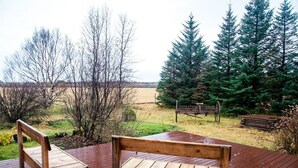 A wooden deck with two benches overlooking a natural landscape with trees and a grassy field. - Kot Guesthouse (Hvolsvöllur)
