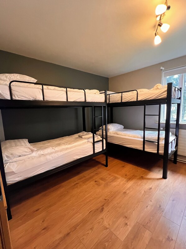 A bunk bed room with wooden flooring and a window with a view of trees.