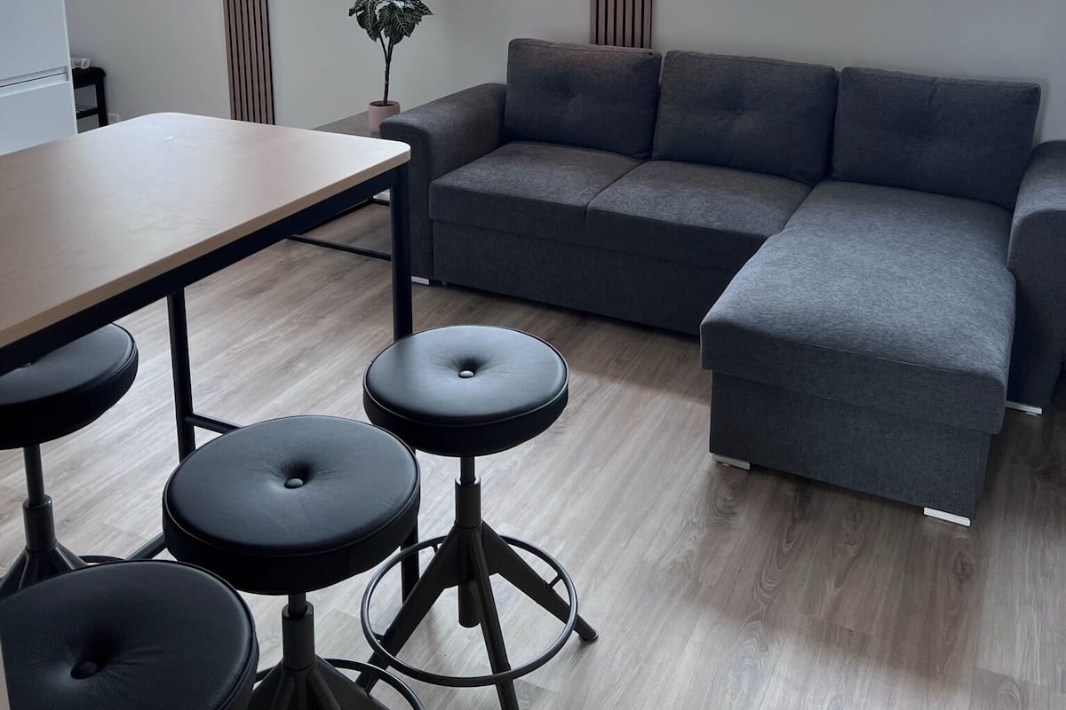 A modern interior with a grey sectional sofa, a wooden dining table, and black stools.
