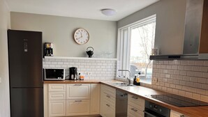 A modern kitchen with white cabinets, a stainless steel refrigerator, a microwave, and a coffee maker. - Kot Guesthouse (Hvolsvöllur)