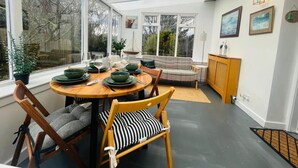 Uma sala de jantar com mesa redonda, cadeiras e um banco. Há janelas, um sofá e um armário.