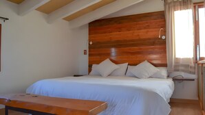 Una camera da letto con una testiera in legno, un letto con biancheria bianca, un comodino e una finestra con tende.