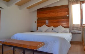 Un dormitorio con cabecera de madera, cama con ropa blanca, mesita de noche y ventana con cortinas.