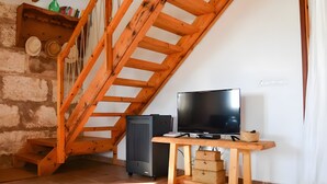Una stanza con una scala in legno, un televisore su un mobiletto in legno e un tavolino con un cesto.