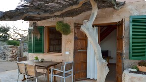 Un'area salotto esterna rustica con tavolo e sedie, una porta in legno e un muro di pietra sullo sfondo.
