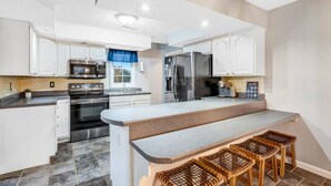 Una cucina moderna con mobili bianchi, elettrodomestici in acciaio inossidabile, un'isola centrale con sgabelli e un pavimento piastrellato.