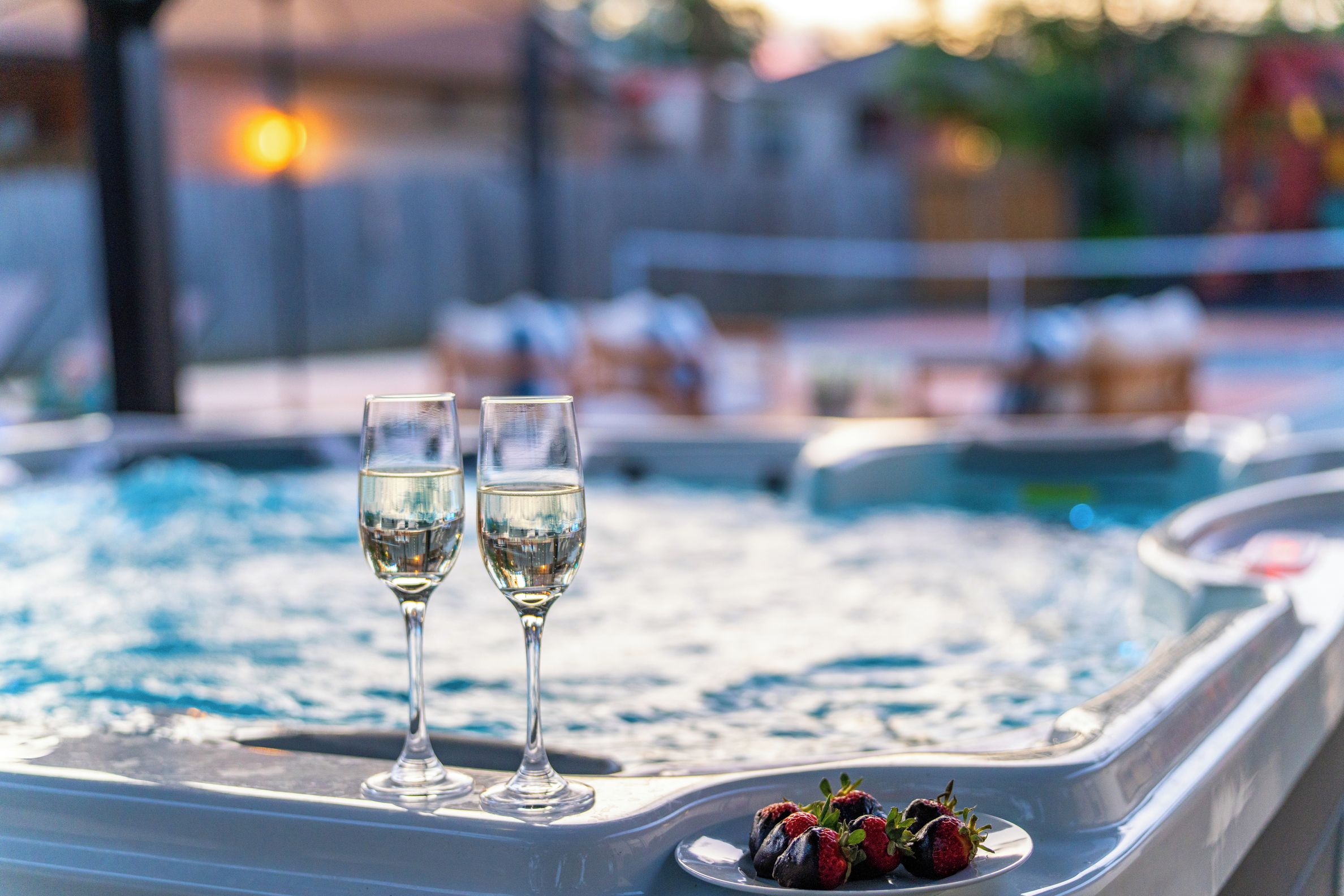 Un jacuzzi con dos copas de vino blanco y un plato de fresas.