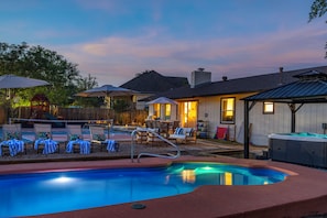Een achtertuin met een zwembad, lounge stoelen, een barbecuehoek en een jacuzzi.