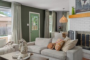 Een woonkamer met een groene deur, een bank met opvallende kussens, een hanglamp en een open haard.