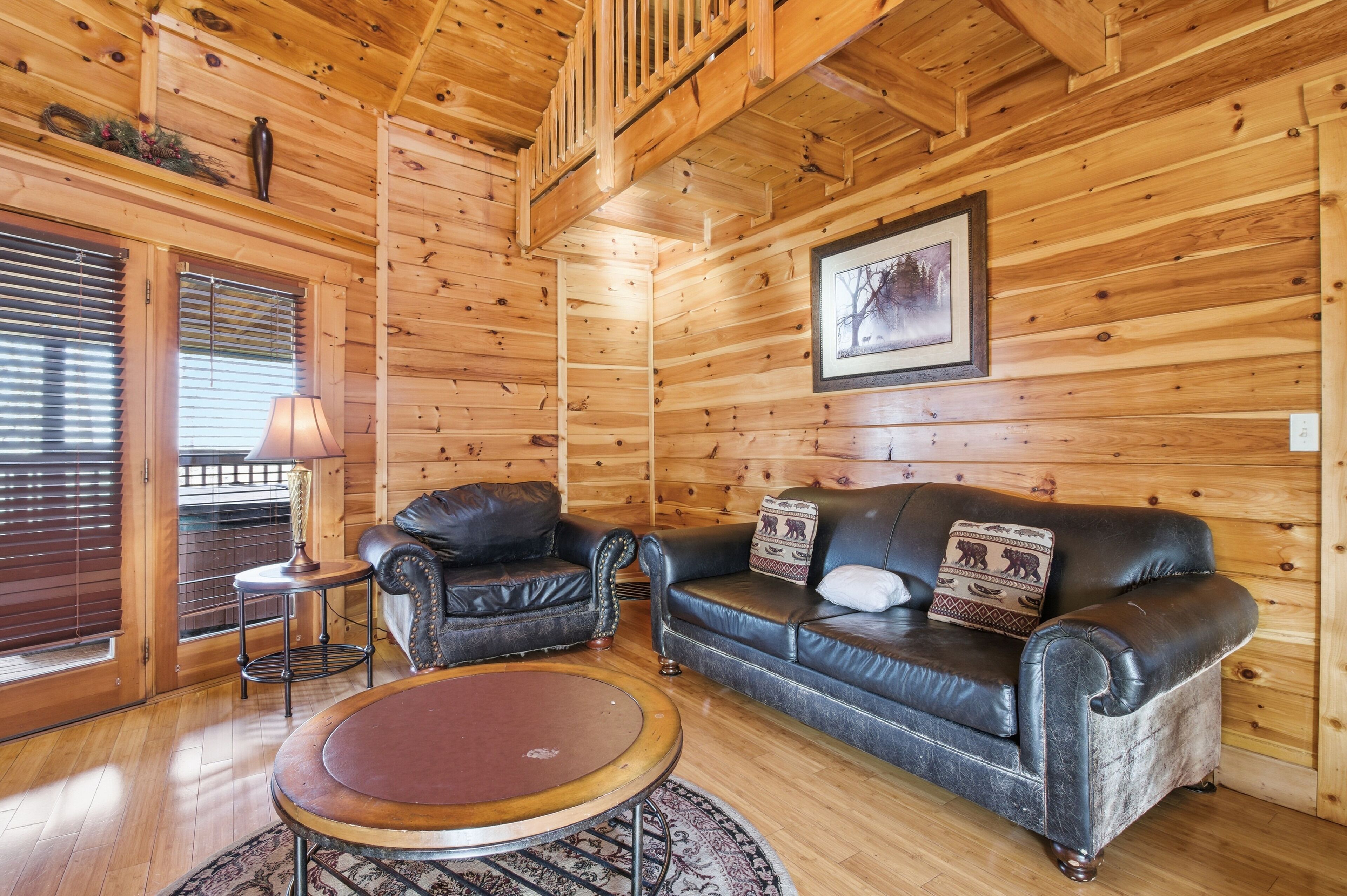 L’intérieur d’une cabane en rondins, avec un canapé en cuir, une table basse ronde et un tableau encadré au mur.