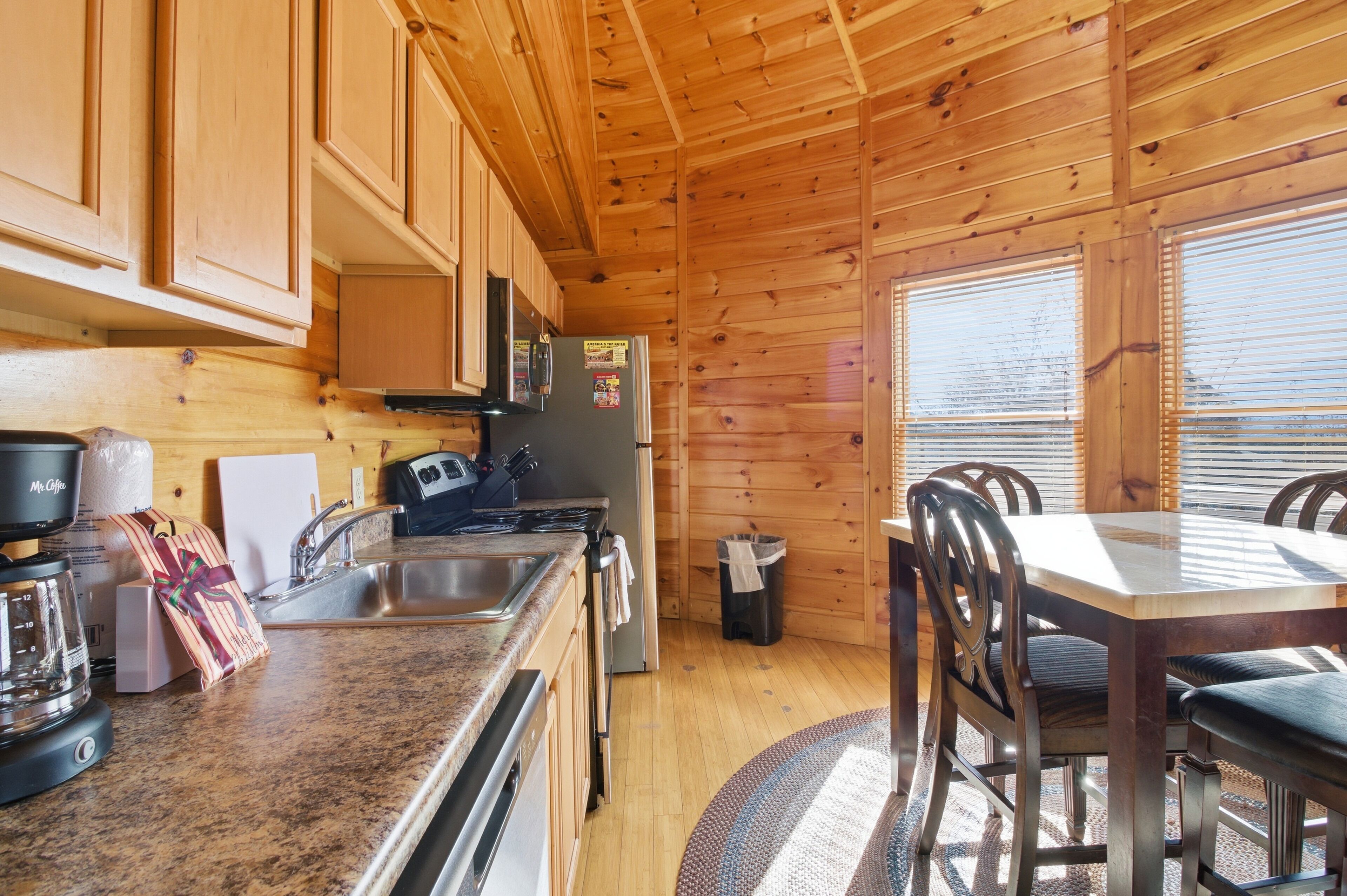 A wooden cabin kitchen with granite countertops, a stainless steel sink, a refrigerator, and a dining table with chairs.