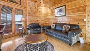 A wooden cabin interior with a leather sofa, a round coffee table, and a framed picture on the wall. - Just Hanging Around (Sevierville)
