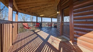 A wooden deck with a covered area, red chairs, and a wooden door. - Just Hanging Around (Sevierville)