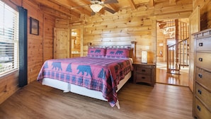 A wooden cabin bedroom with a bed, a nightstand, a dresser, and a ceiling fan. - Just Hanging Around (Sevierville)