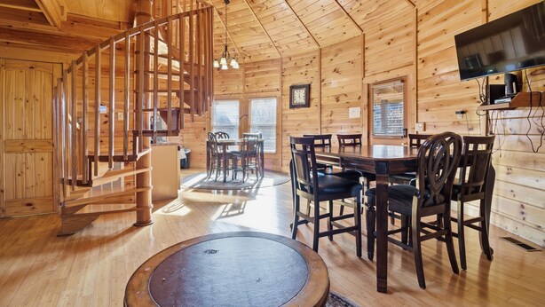 A wooden cabin interior with a dining area, a staircase, and a flat-screen TV mounted on the wall. - Just Hanging Around (Sevierville)