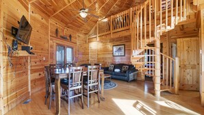 A wooden cabin interior with a dining area, a sofa, a staircase, and a ceiling fan. - Just Hanging Around (Sevierville)