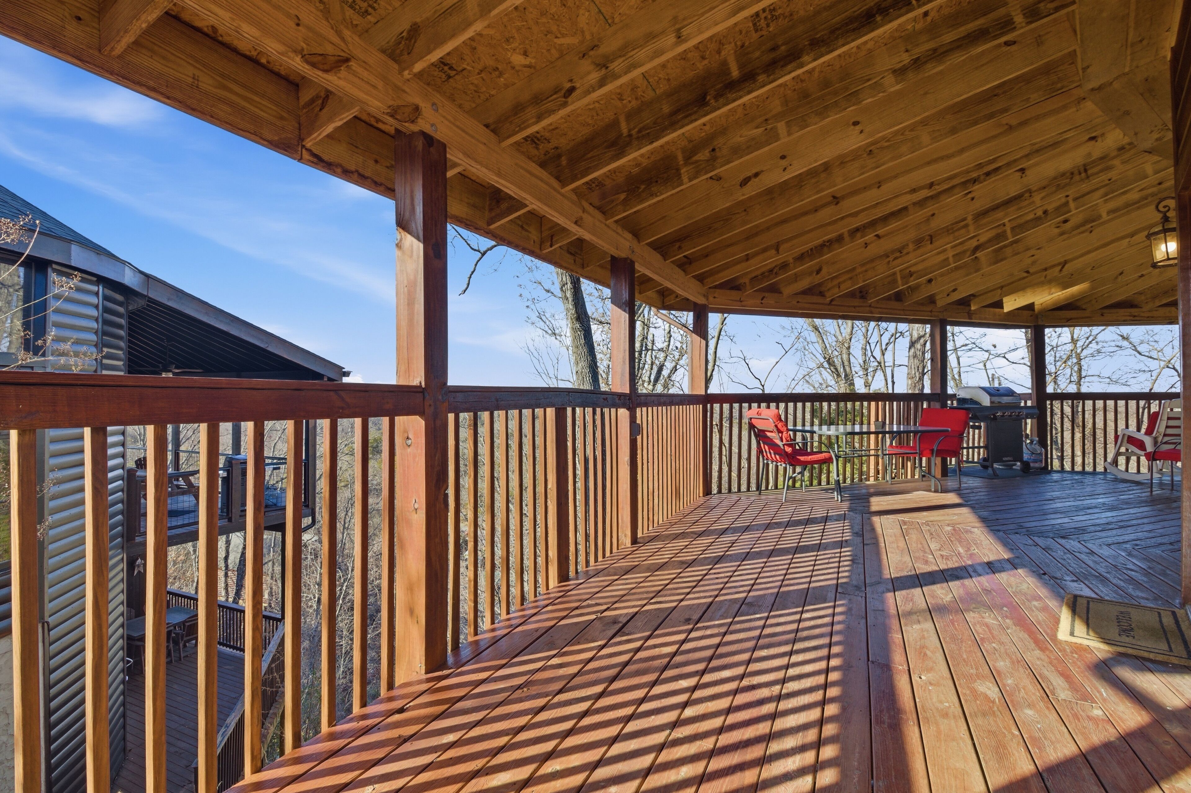 A wooden deck with a railing, red chairs, and a grill area.
