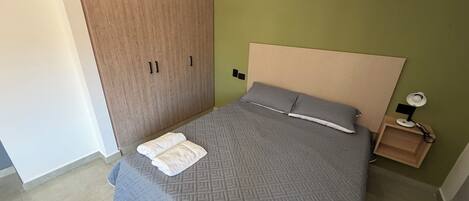 A bedroom with a bed, a nightstand, a wooden wardrobe, and an air conditioning unit.