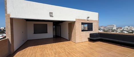 A rooftop terrace with a wooden floor, a small brick structure, and a window.