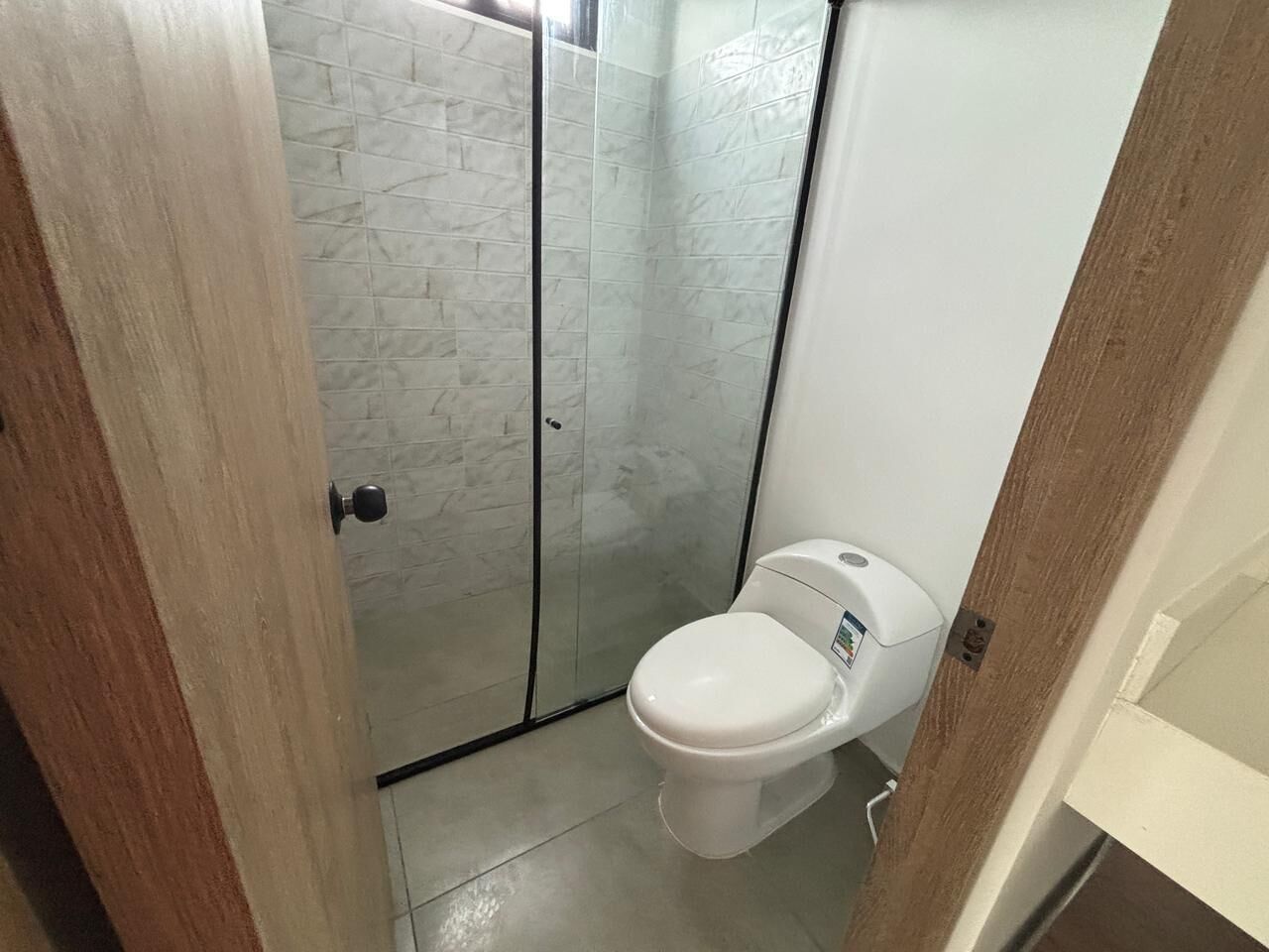 A bathroom with a glass shower enclosure, a white toilet, and a tiled floor.