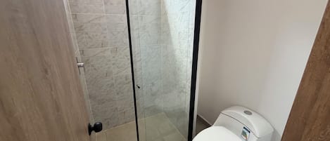 Ein Badezimmer mit Duschkabine, Toilette und einer Tür zu einem weiteren Raum.
