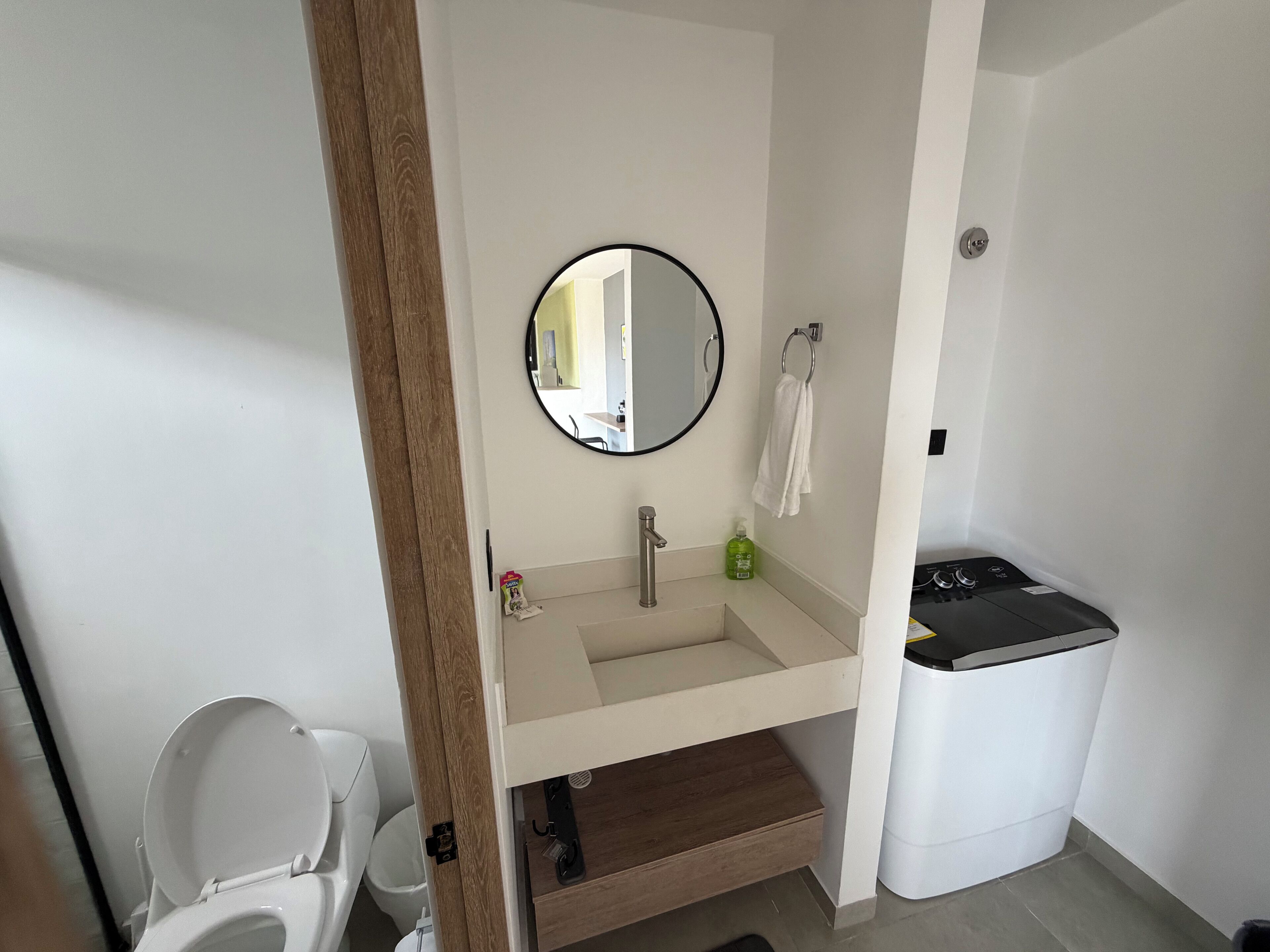 A bathroom with a toilet, sink, mirror, and a trash bin.