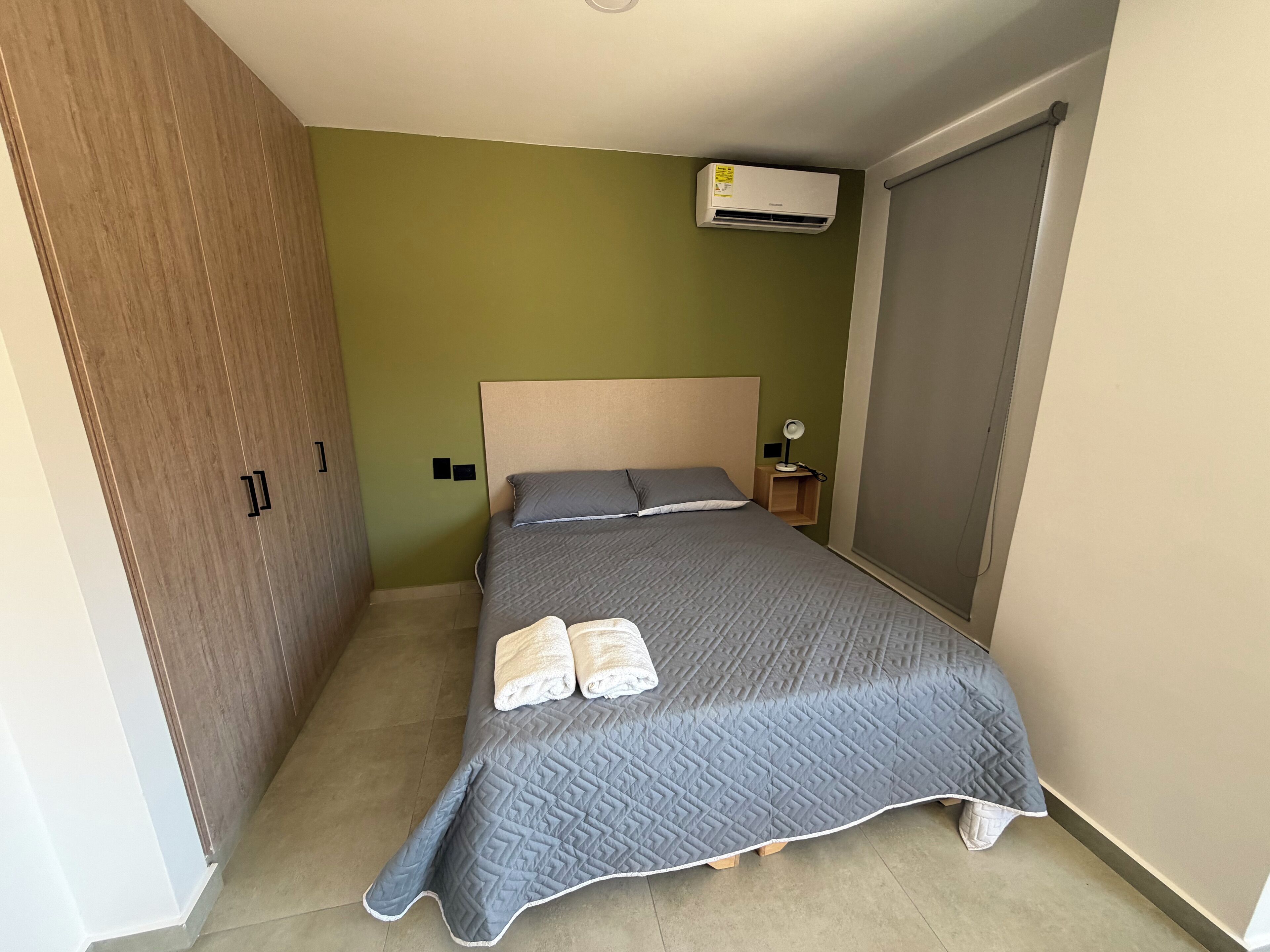 A bedroom with a bed, a nightstand, an air conditioning unit, and a wardrobe.