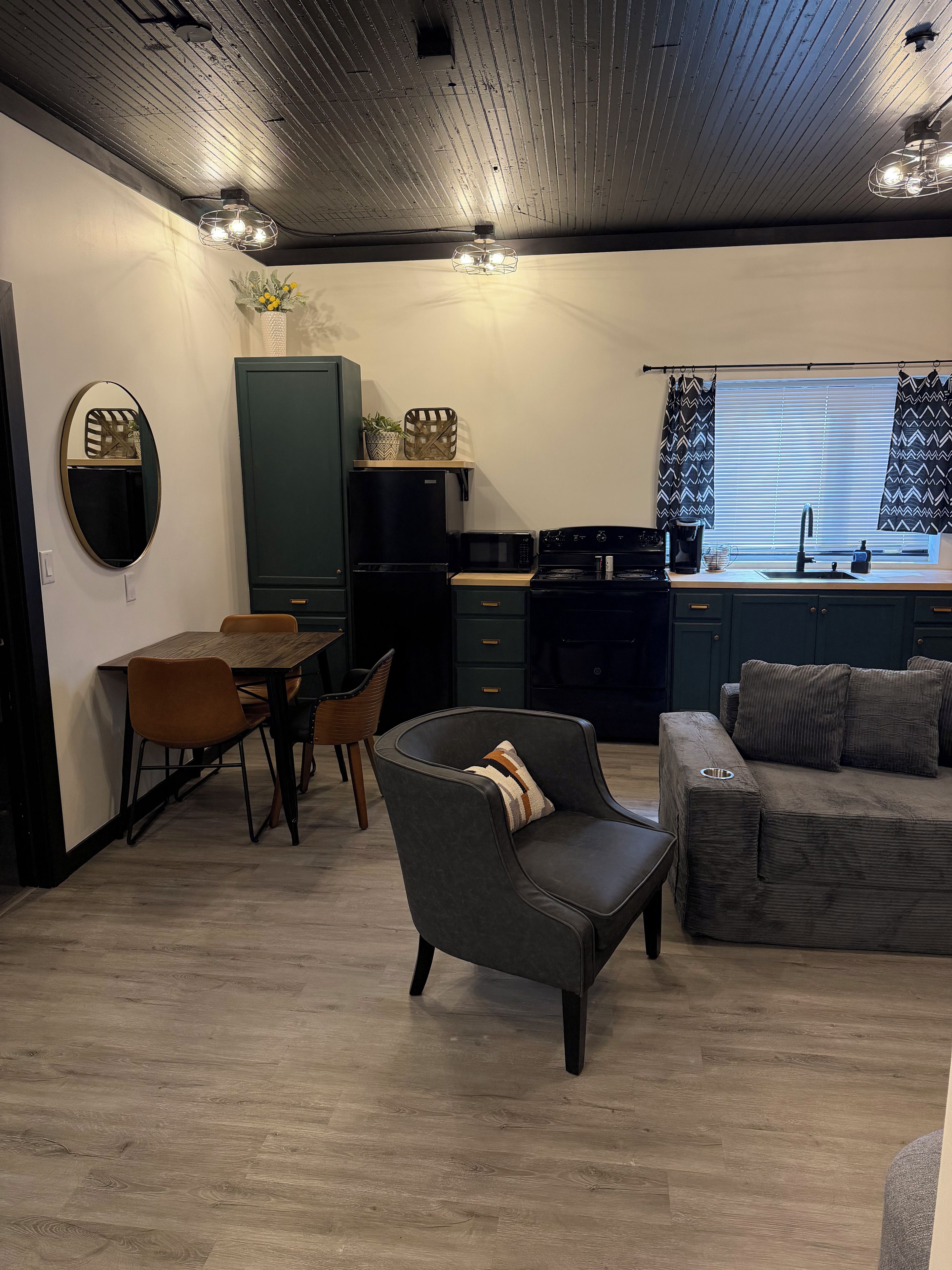 Un salon moderne comprenant un canapé, une table à manger avec des chaises, un coin cuisine équipé d’appareils électroménagers et une fenêtre avec des rideaux.