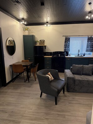 Un salon moderne comprenant un canapé, une table à manger avec des chaises, un coin cuisine équipé d’appareils électroménagers et une fenêtre avec des rideaux.