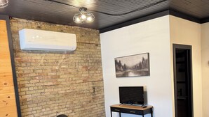 Una sala de estar moderna con una pared de ladrillo, un televisor de pantalla plana, una mesa de centro de madera y muebles negros y grises.