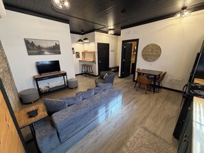 A modern living room with a grey sofa, a TV, and a dining area with a table and chairs.