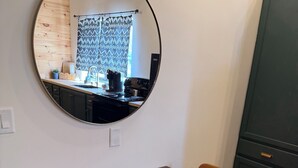 Un comedor con un espejo redondo, una mesa de madera, dos sillas y una cocina visible a través del espejo.
