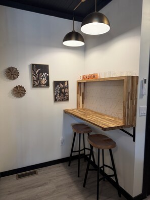 Eine Bar mit einer Holztresen, zwei Barhocker, Pendelleuchten und Wanddekorationen.