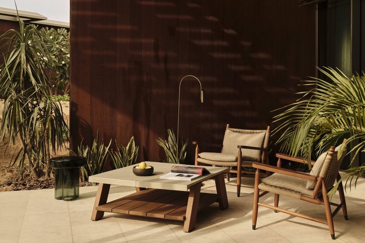 An outdoor seating area with a wooden table, two chairs, a floor lamp, and potted plants.