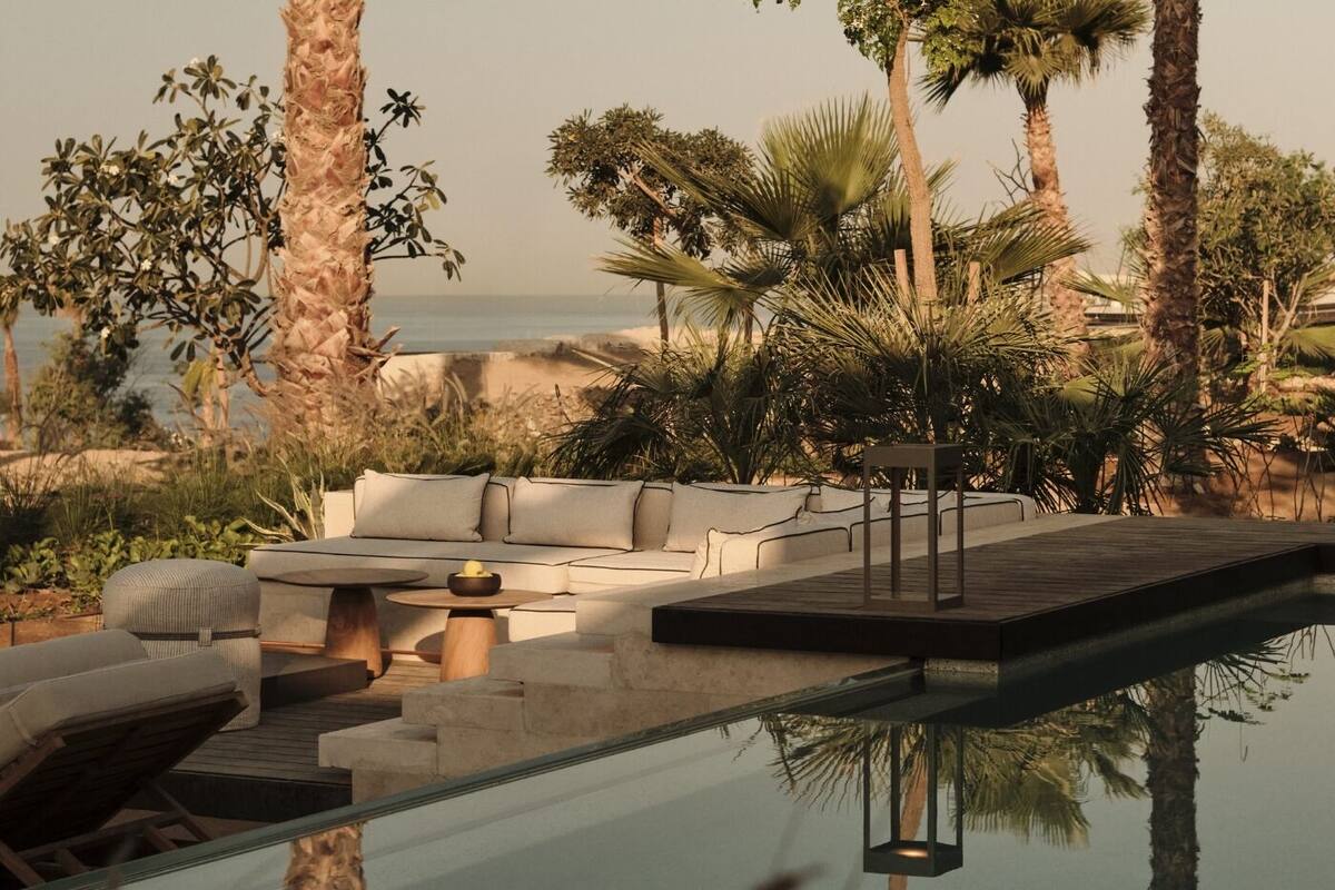 A modern outdoor seating area with a glass-top pool, surrounded by palm trees and a view of the ocean.