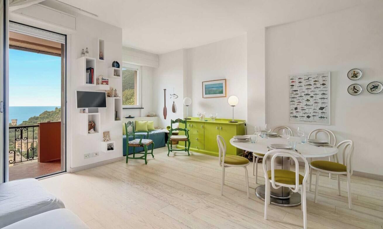 Ein modernes Wohnzimmer mit Balkon, einem Essbereich mit einem grünen Schrank und einem an der Wand befestigten Fernseher.