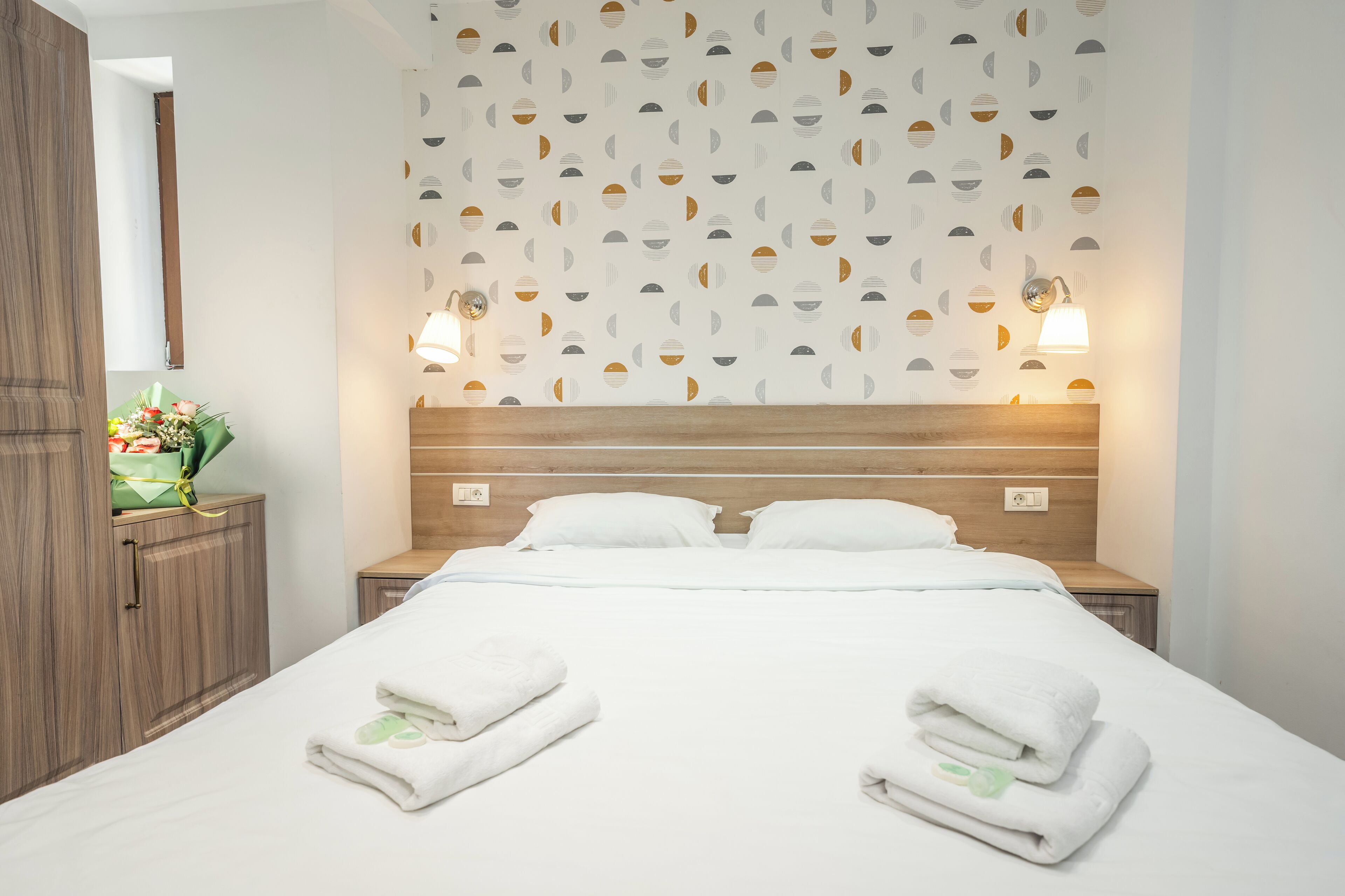 A neatly made bed with white linens and towels, a wooden headboard, and a wall with a geometric pattern.