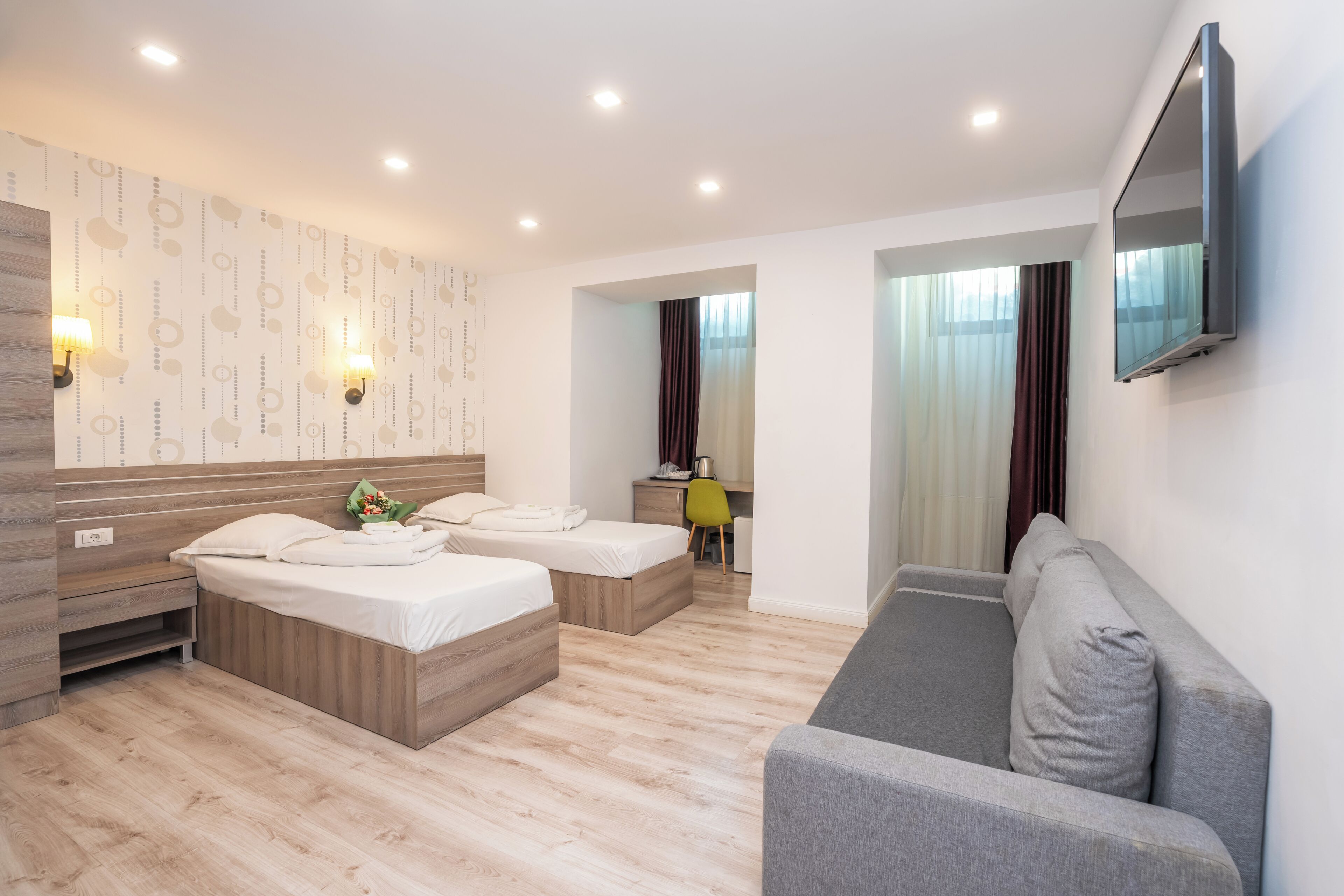Une chambre d’hôtel moderne équipée de deux lits, d’un canapé, d’une télévision à écran plat et d’un bureau avec une chaise.