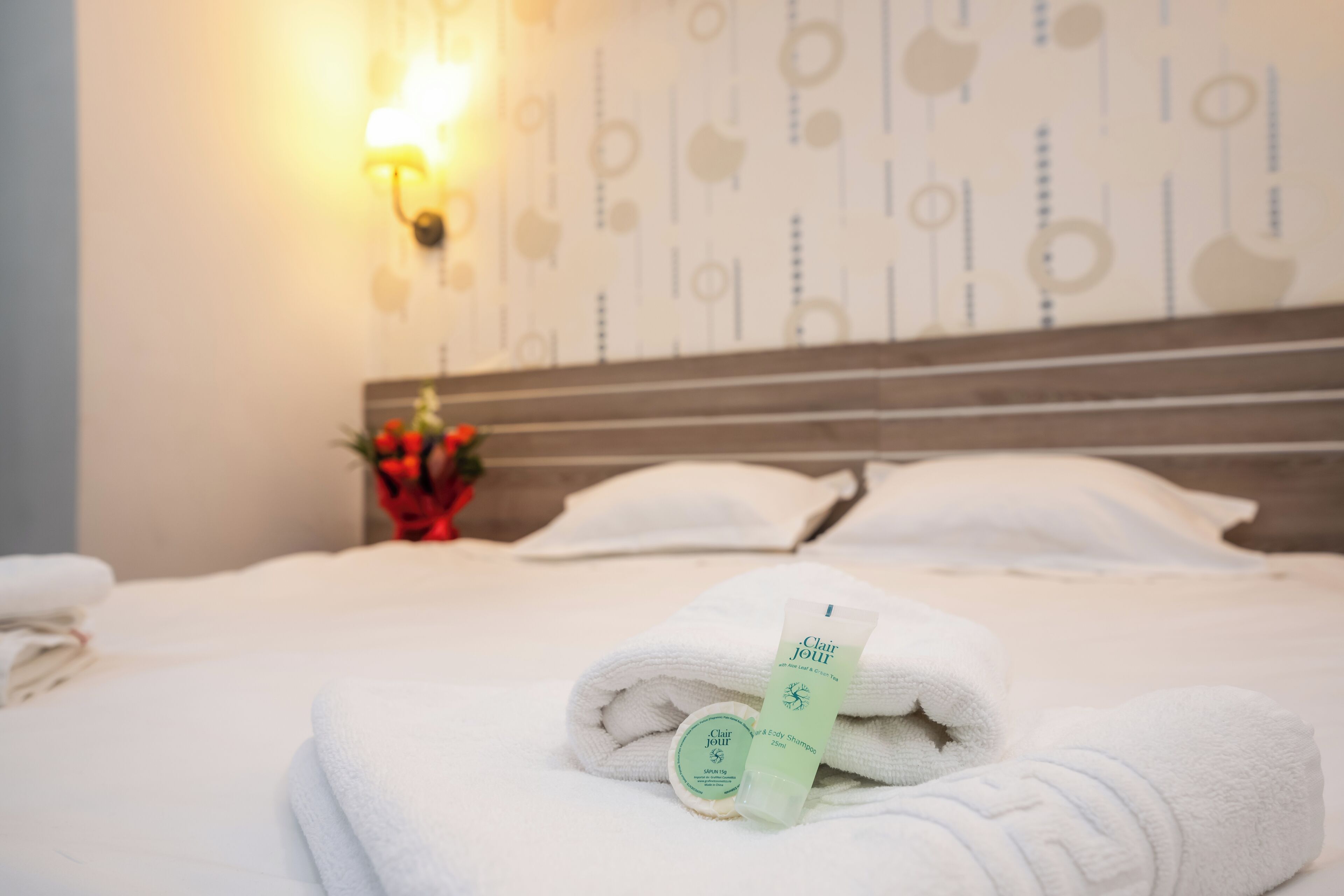 A neatly made bed with white towels and a bottle of hair and body wash.