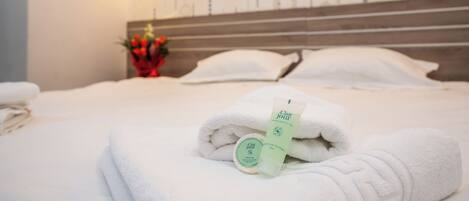 A neatly made bed with white towels and a bottle of hair and body wash.