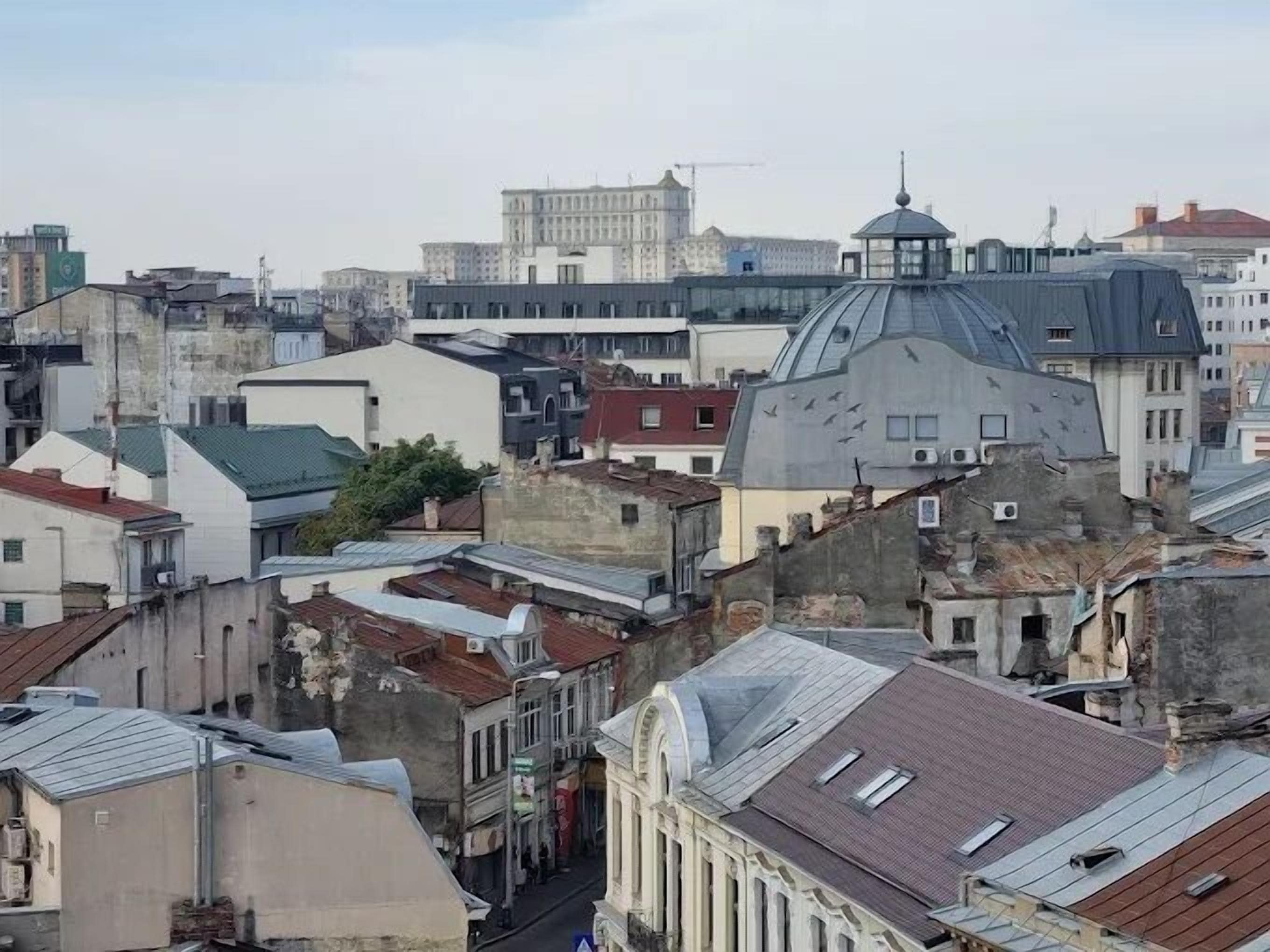 Une zone urbaine densément peuplée, avec divers bâtiments, dont une structure imposante surmontée d’un dôme et un bâtiment plus petit doté d’un toit plat.
