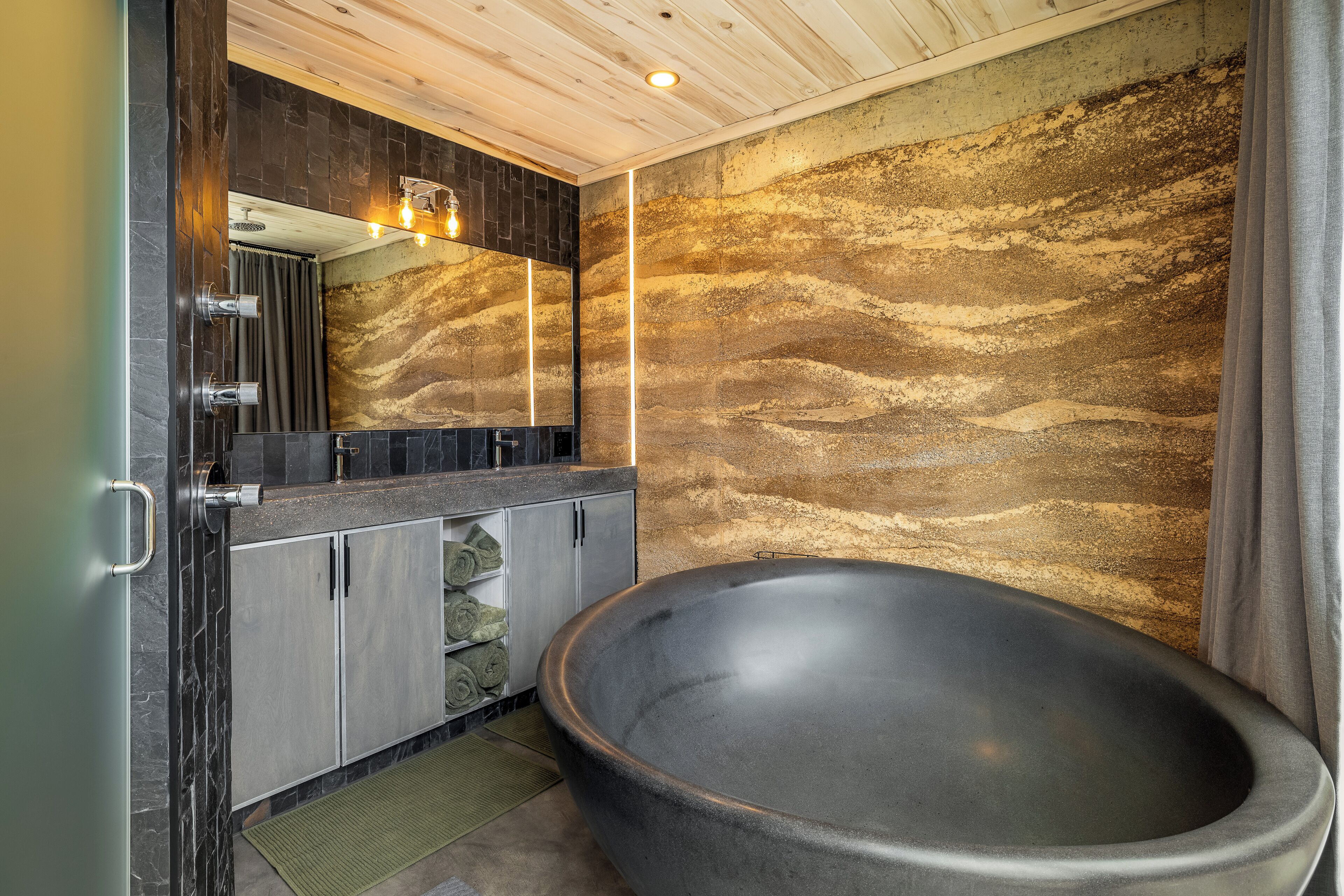 Une salle de bain moderne avec une baignoire sur pieds, des plans de toilette en marbre foncé et un mur en pierre à texture.