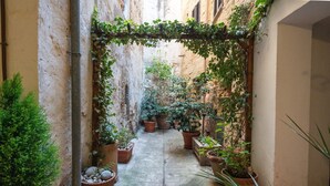 Une ruelle étroite, bordée de plantes en pot et surmontée d’une grille métallique au niveau du sol.