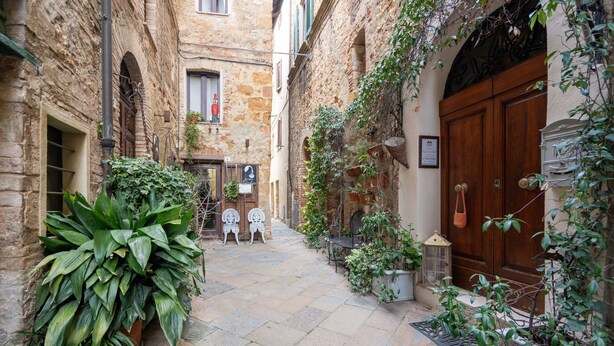 Une ruelle étroite aux murs de pierre, ornée de plantes en pot et dotée d’une porte en bois.